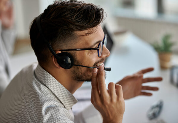 Happy call center agent wearing headset while talking with clients and working in the office.